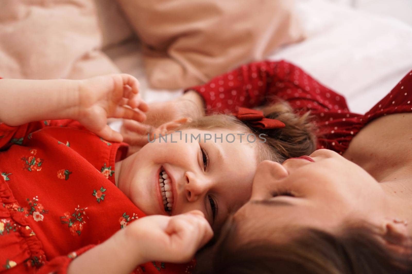 Mom and her little daughter lie on the bed facing each other. They are happy by natali_brill