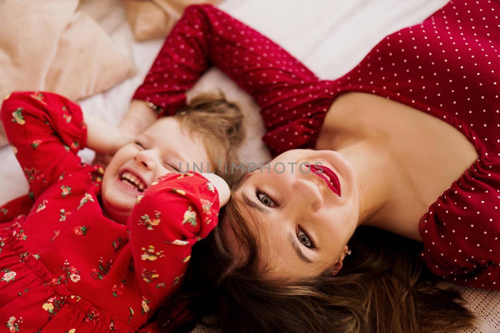 Mom and her little daughter lie on the bed facing each other. They are happy by natali_brill