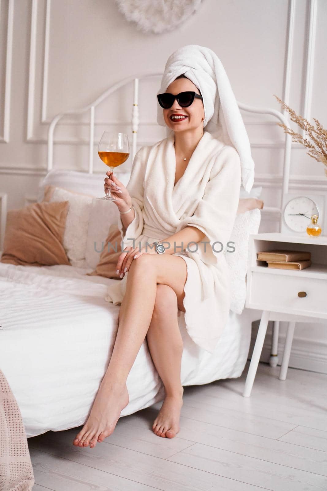 Woman in a white bathrobe, towel and sunglasses. She is holding a glass of wine by natali_brill