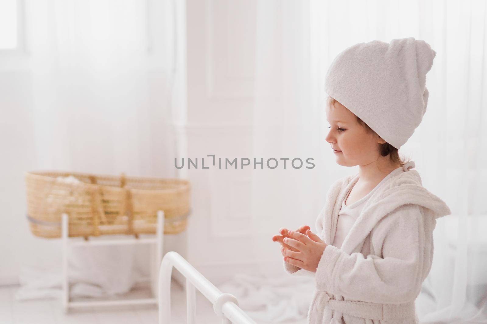 Smiling little girl in a white bathrobe after a bath. White cozy interior. Hygiene and baby fashion concept