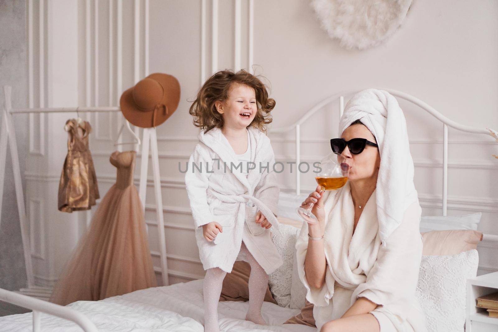 Mother and daughter in the bedroom in bathrobes. Happy daughter is jumping by natali_brill