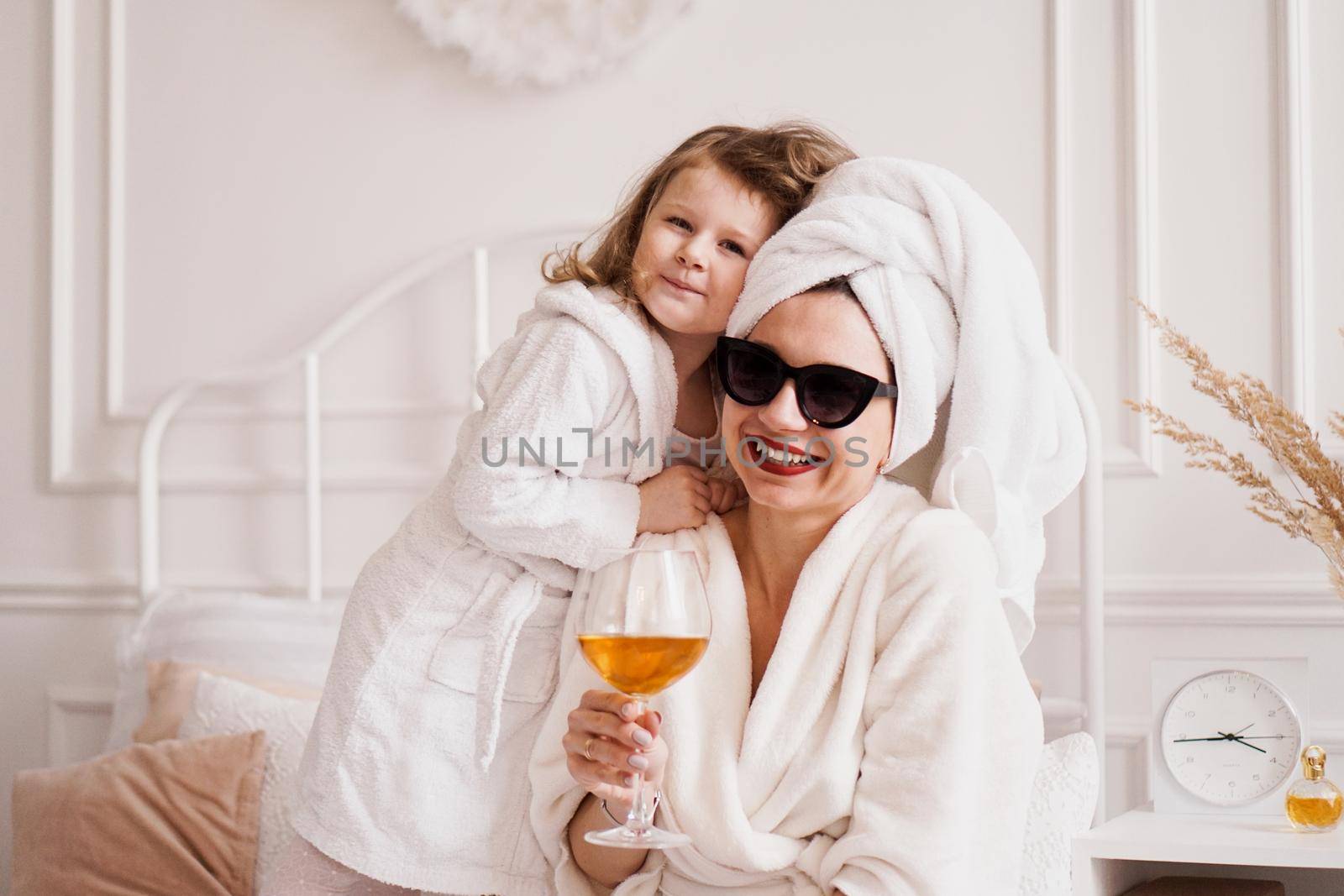 Mother and daughter in the bedroom in bathrobes. The girl hugs her mom by natali_brill