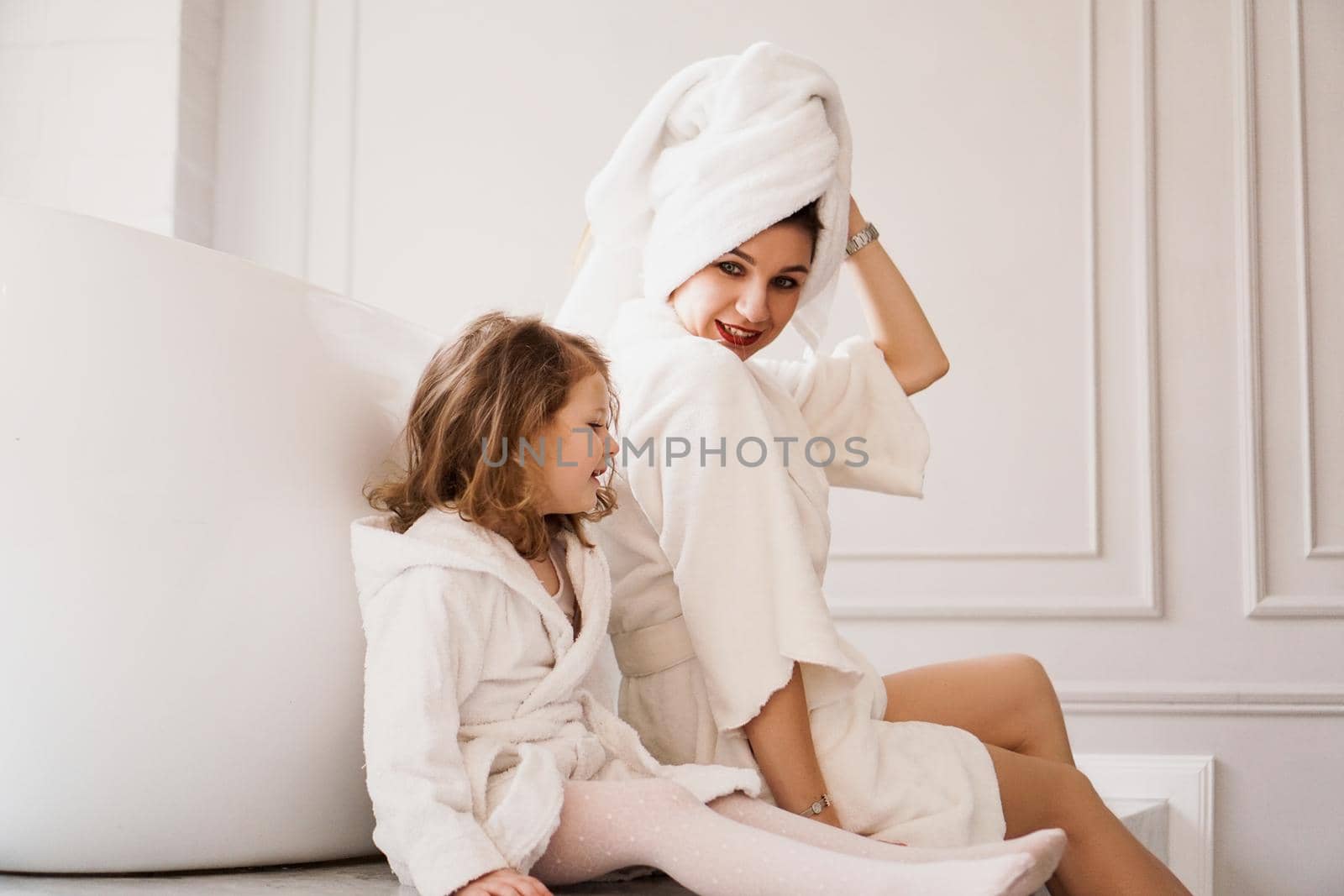 Mother and daughter in white coats in light bathroom. by natali_brill
