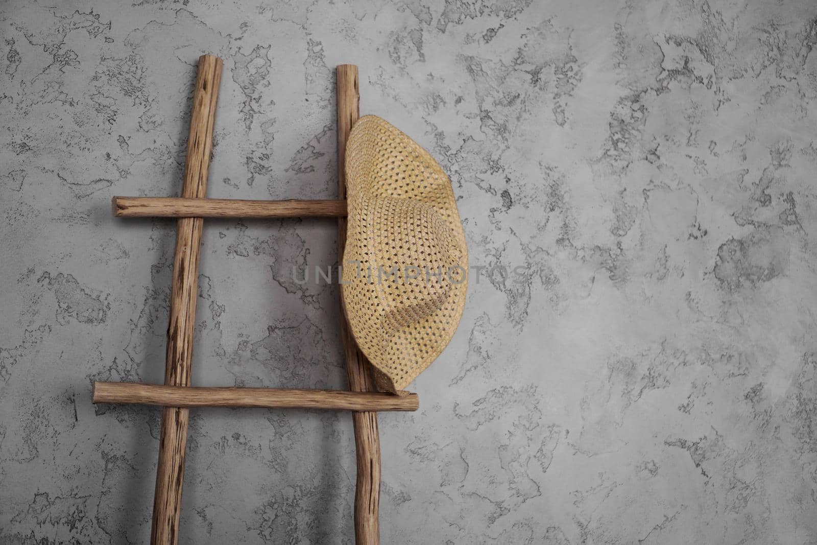 Wall with rough plaster. On the wall is an old wooden staircase. A wicker straw hat on a rustic staircase. Country style