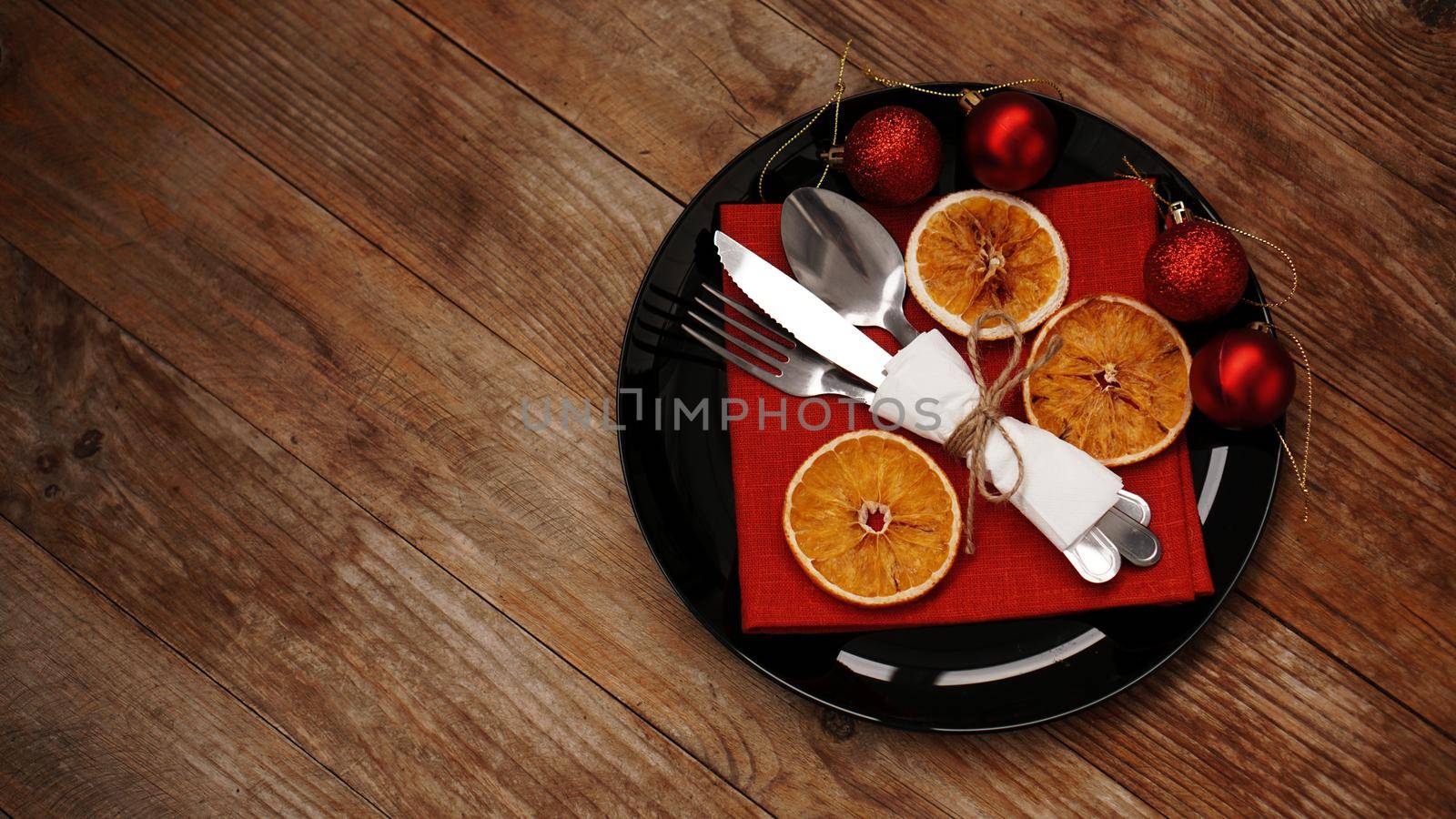 Christmas dinner decoration with dried oranges and a red napkin on a black plate on wooden background. Space for text