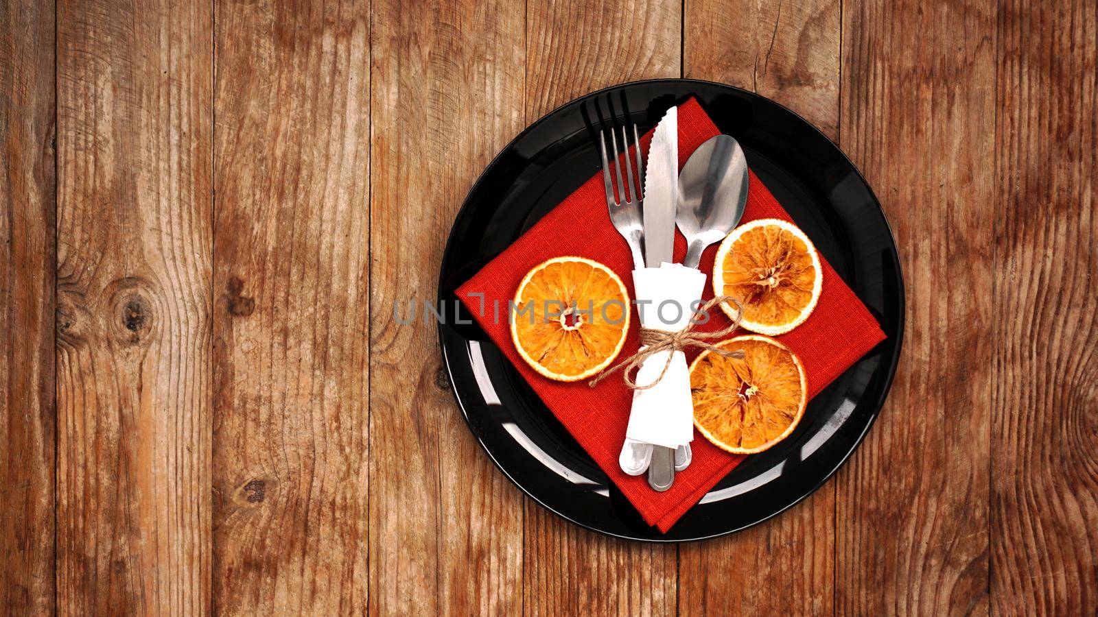 Christmas dinner decoration with dried oranges and a red napkin on a black plate on wooden background. Space for text