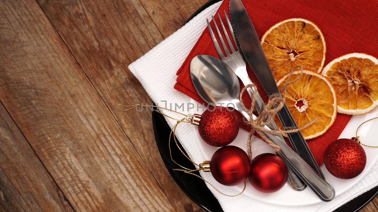 Christmas dinner decoration with dried oranges and red and white napkins on a black plate on wooden background. Space for text