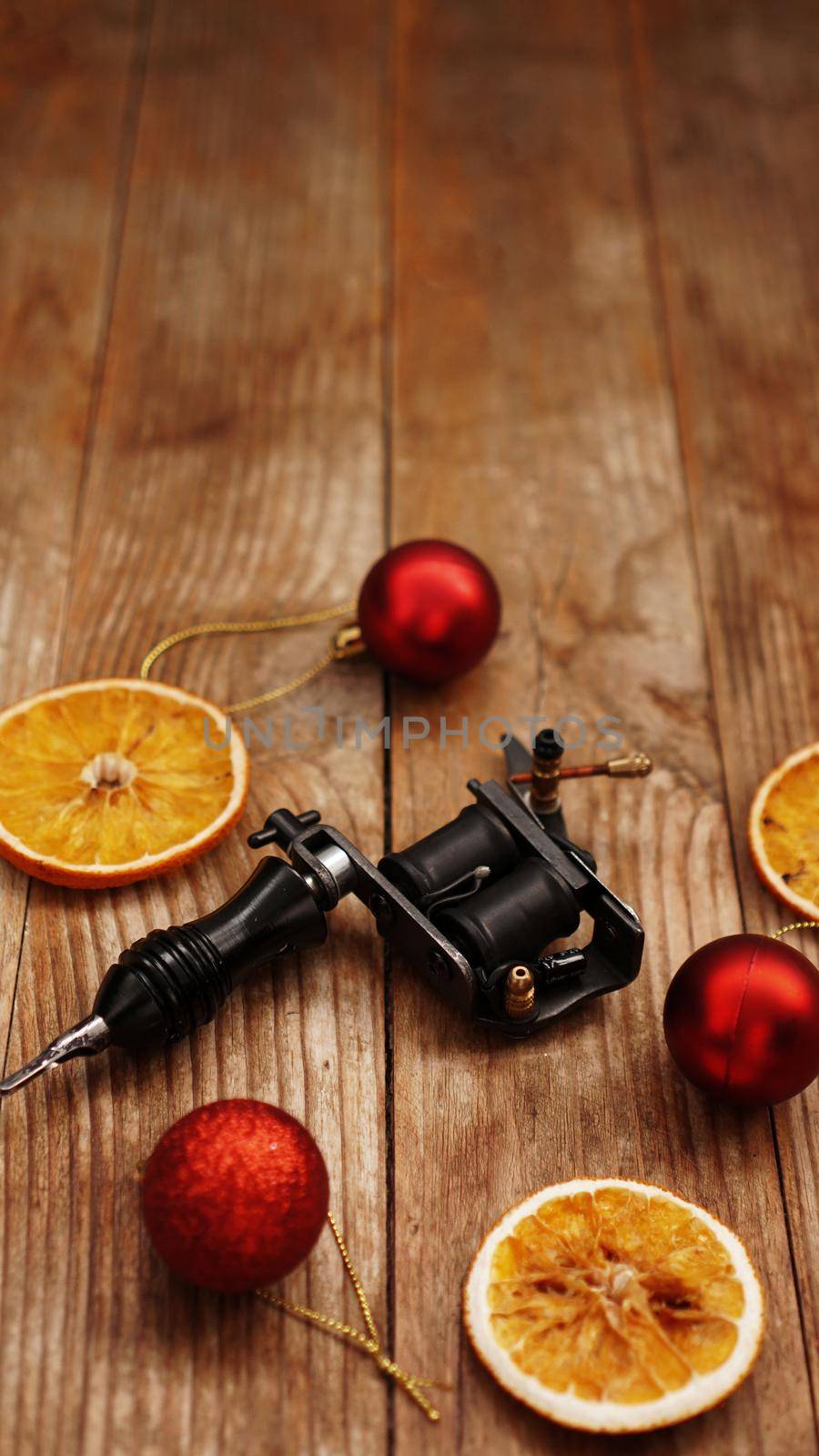 Tattoo machines on a christmas background - christmas decor with red balls and dried oranges on a wooden background. Vertical photo