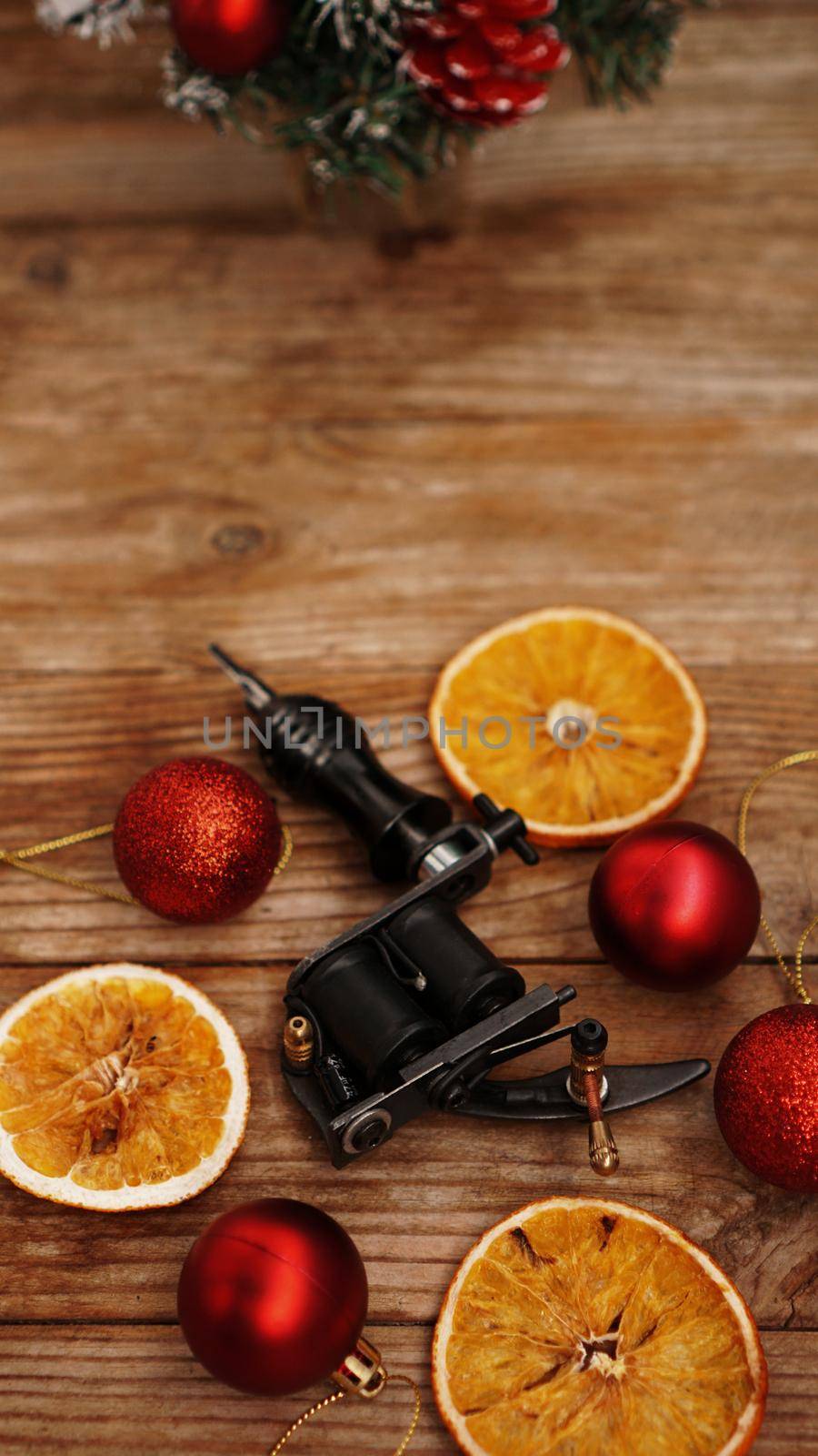 Tattoo machines on a christmas background - christmas decor with red balls and dried oranges on a wooden background. Vertical photo