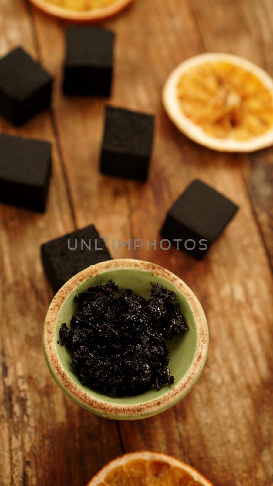 Tobacco in the bowl for hookah on wooden background with coal and dried orange slices. Vertical photo