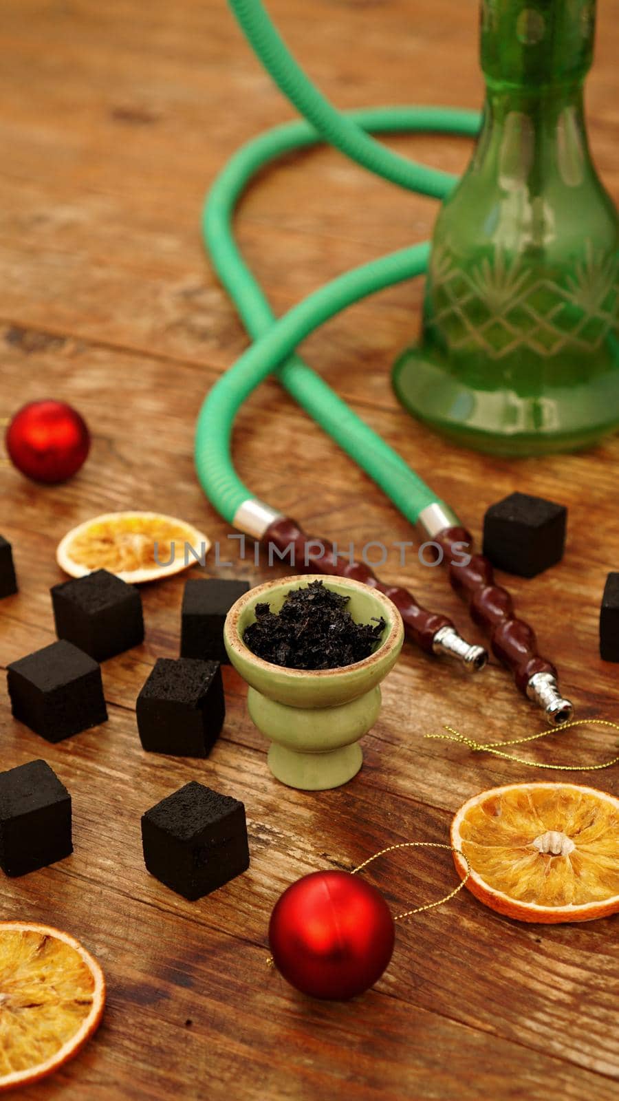 Hookah background for new year and christmas. Hookah, charcoal, dry orange slices and Christmas red balls on a wooden background. Vertical photo