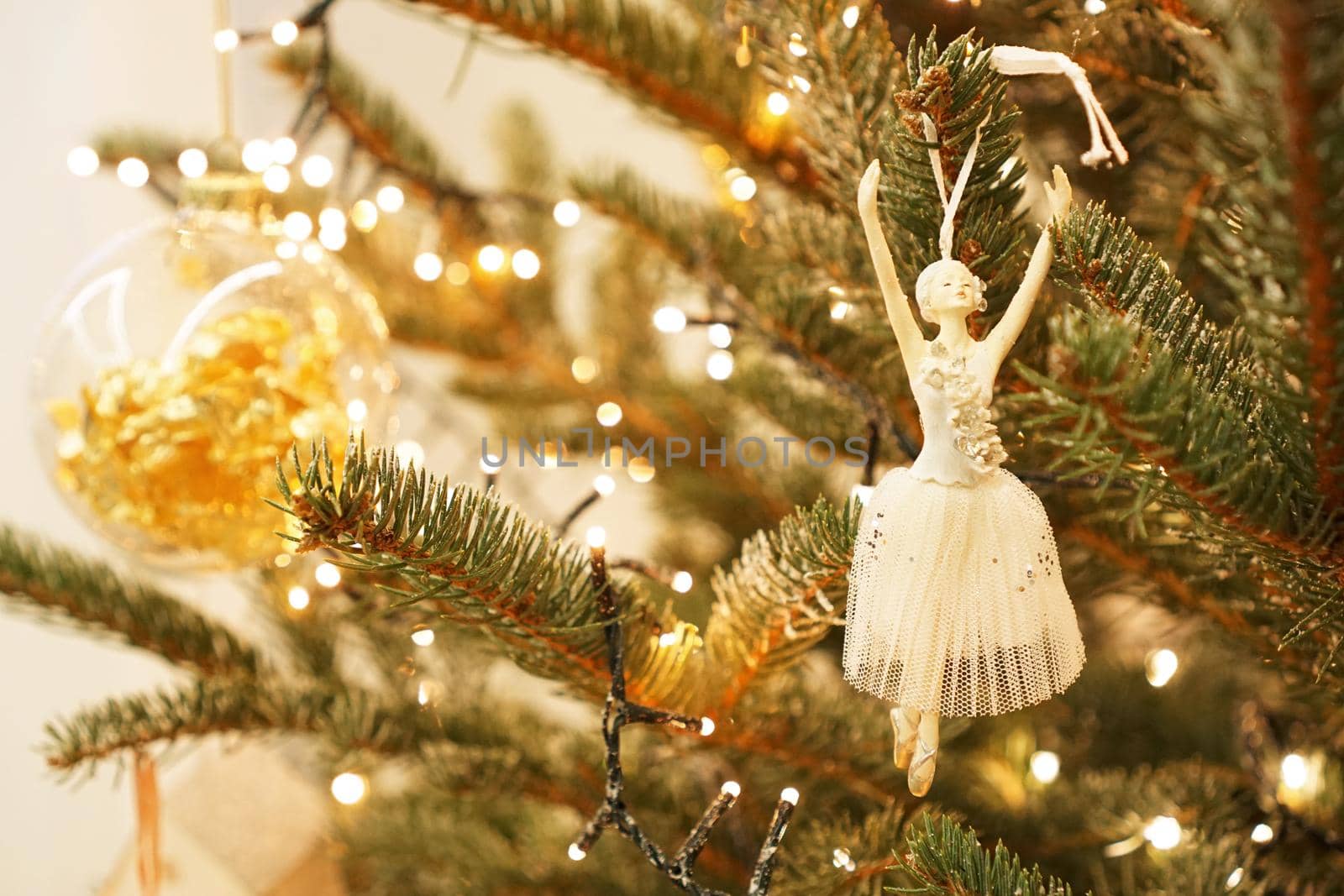 Beautiful ballerina decorates a Christmas tree branch. Festive background of a green Christmas tree and gold balls