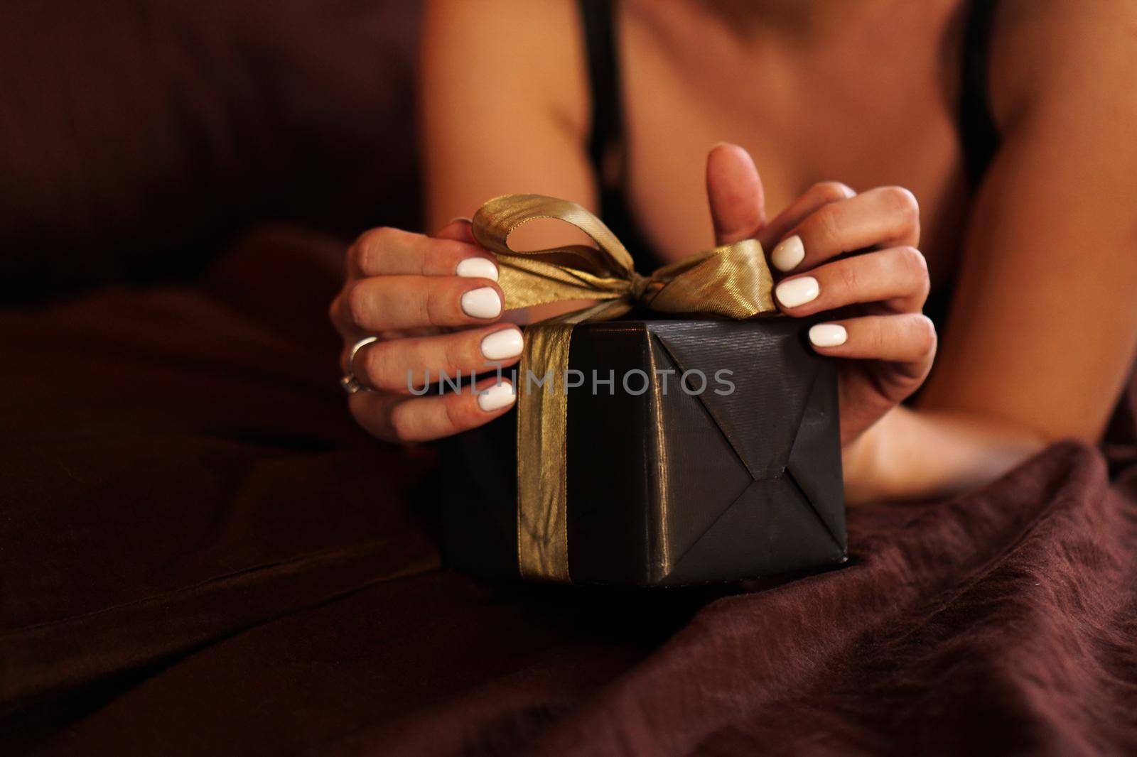 The woman opens a gift in a black box with a gold ribbon. Closeup photo