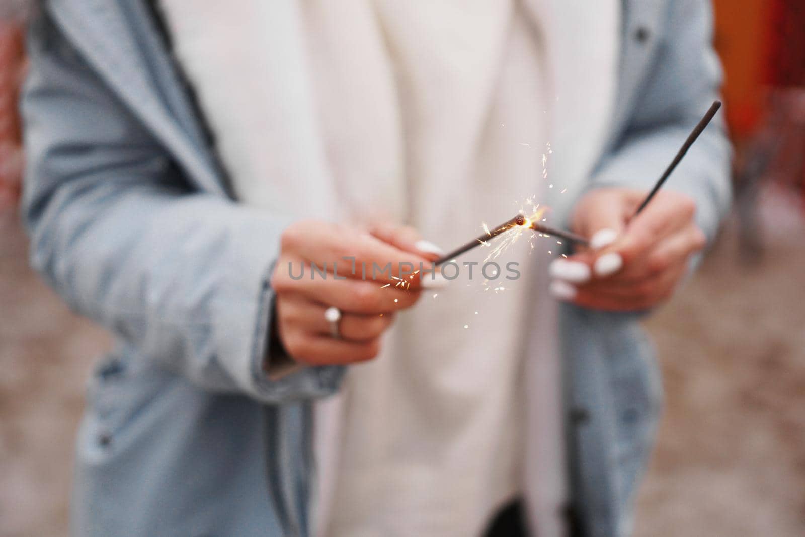 Female hands are holding burning sparklers. Woman outdoors in winter