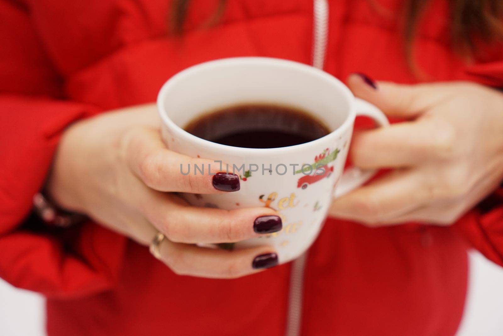 Female hands holding christmas cup with hot dark drink outside on winter day
