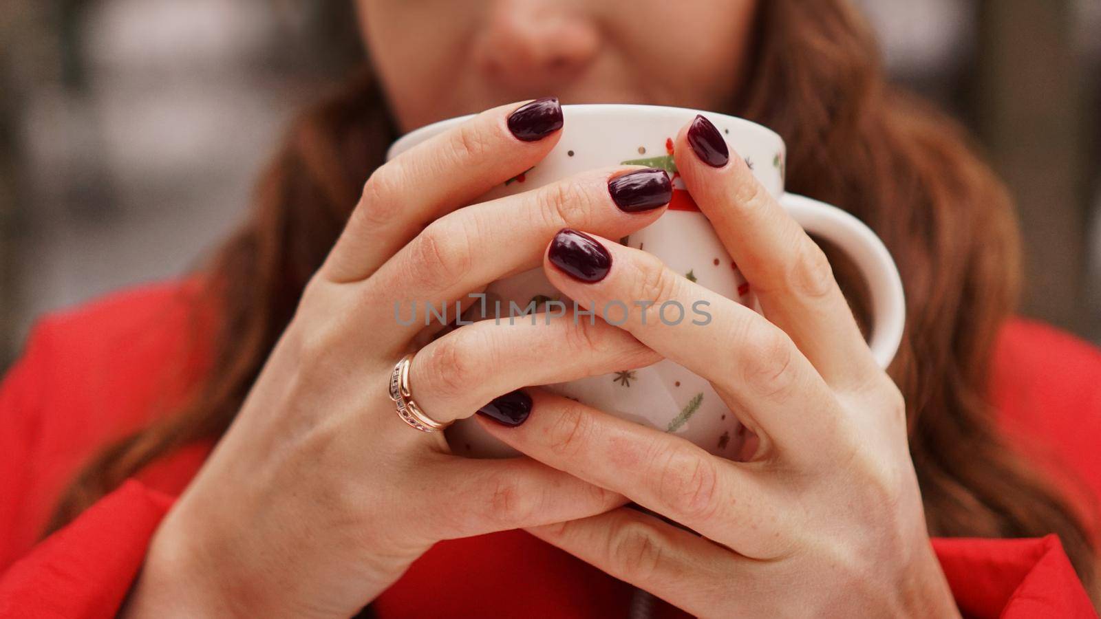 Female hands holding christmas cup with hot dark drink outside on winter day