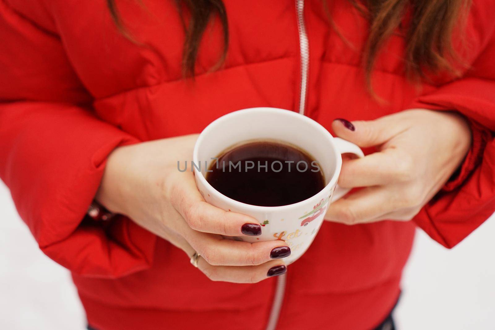 Female hands holding christmas cup with hot dark drink outside on winter day