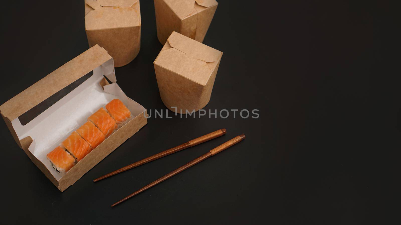 Asian food delivery. Packaging for sushi and woks. Food in paper containers on black background. Open package with salmon rolls