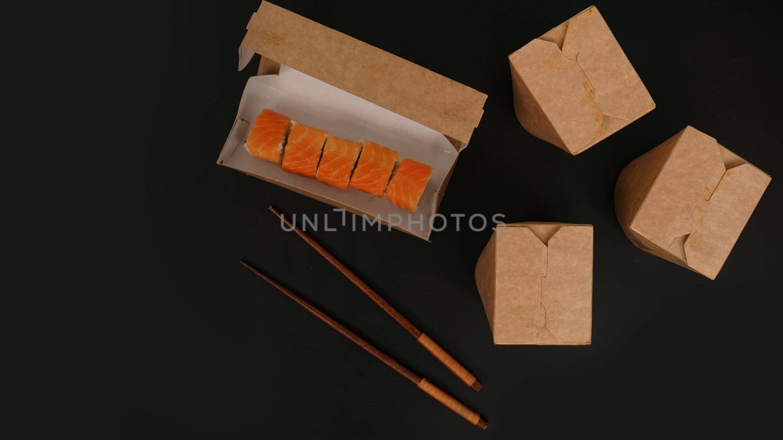 Asian food delivery. Packaging for sushi and woks. Food in paper containers on black background. Open package with salmon rolls