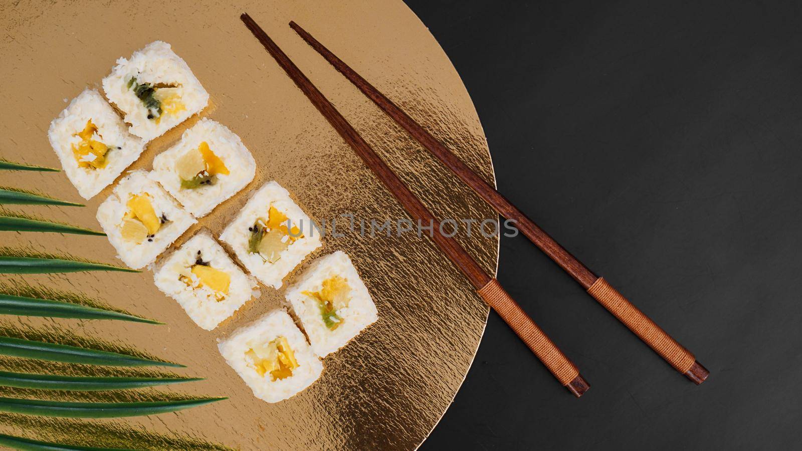 Dessert Sushi - Roll with Various Fruit and Cream Cheese inside. On a gold background and with a tropical leaf