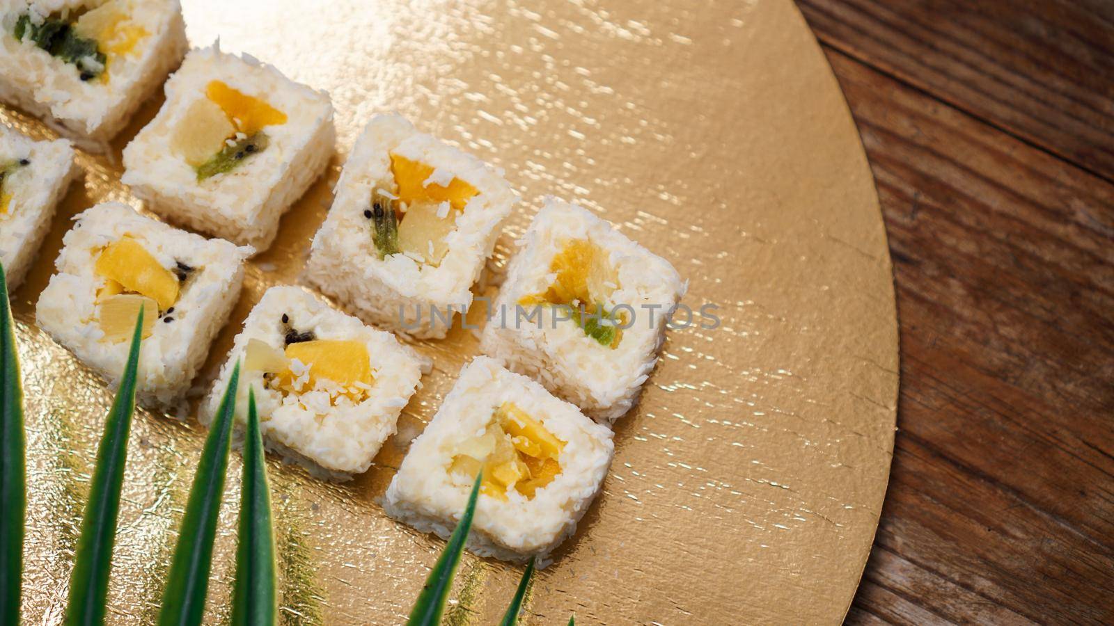 Dessert Sushi - Roll with Various Fruit and Cream Cheese inside. On a gold background and with a tropical leaf