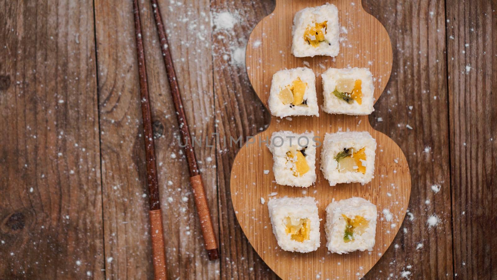 Sushi delivery. Sweet rolls made from rice, pineapple, kiwi and mango. Rolls on a wooden background. Wooden sticks for sushi.