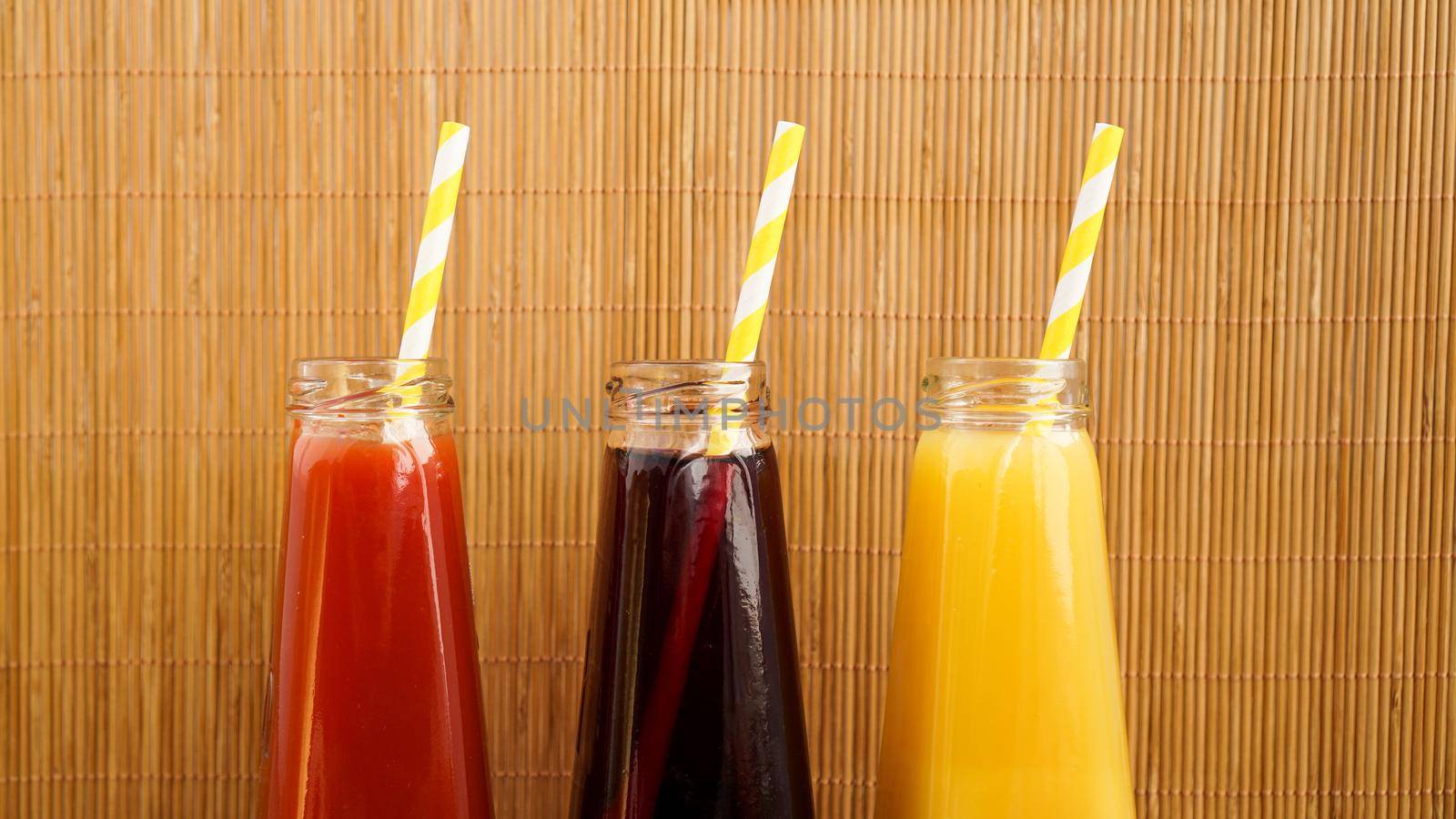 Three multicolored drinks in the bottles on a wooden bamboo background. Bottled paper straws.
