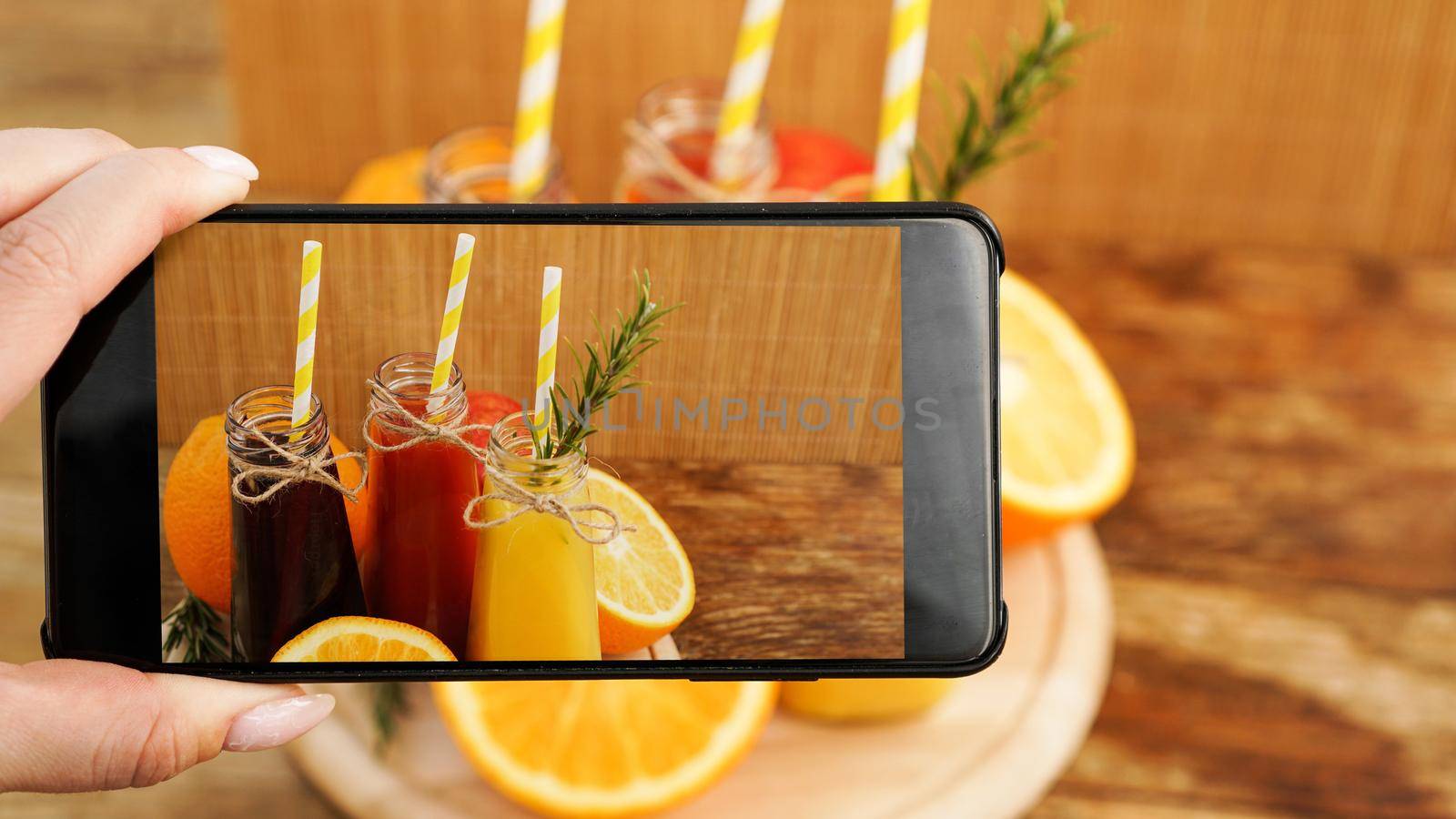 Woman taking picture of fruit juice on her smartphone. Hand holds a phone with a photo. Fruit juices in a bright summer photo. No visible brands and logos