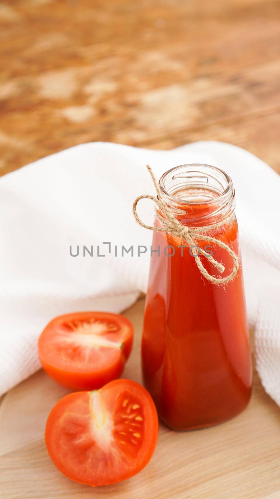 Tomato juice in glass bottle and fresh tomatoes on wooden cutting board and white towel