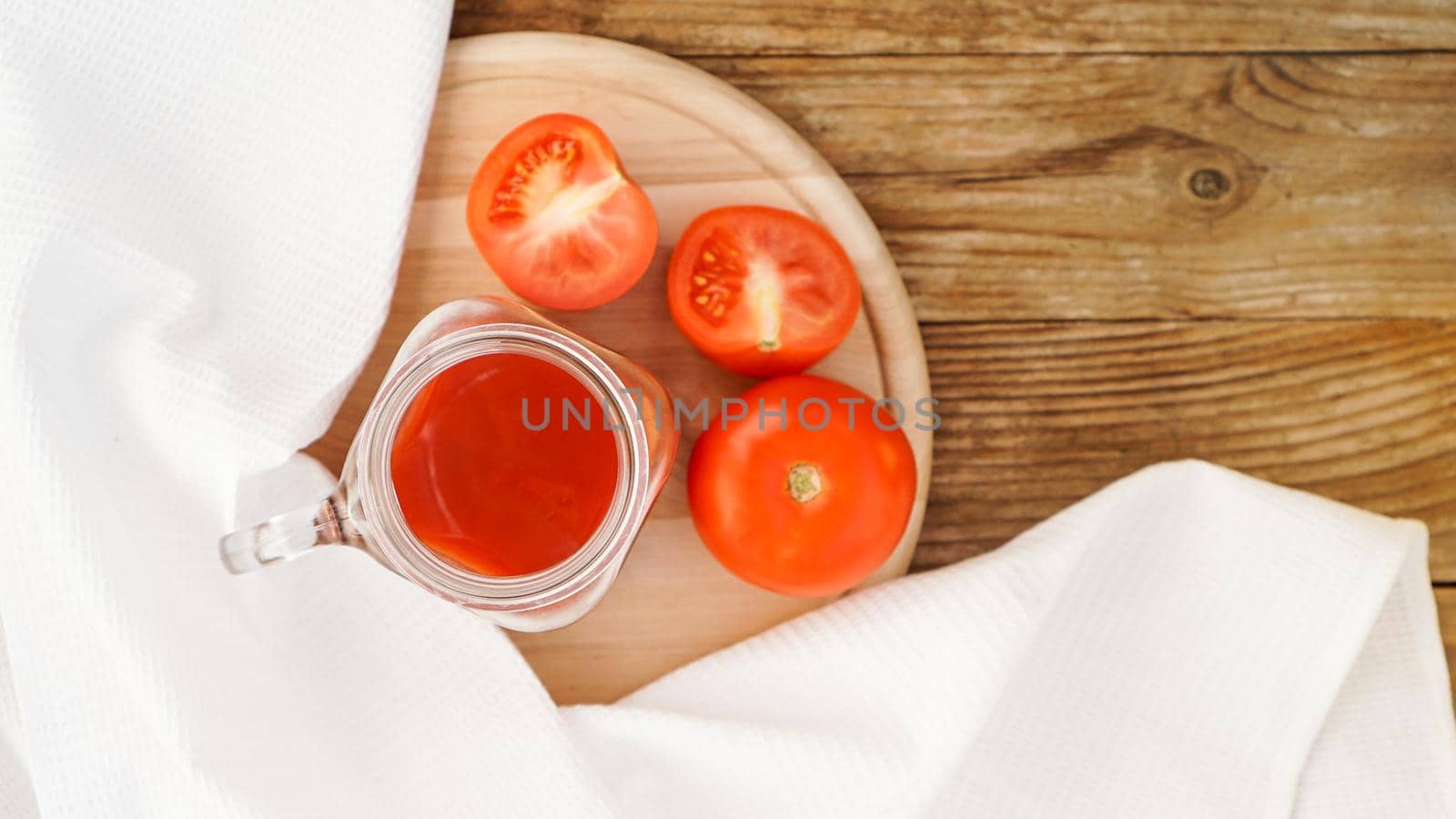 Tomato juice in glass jar and fresh tomatoes on wooden cutting board and white towel - Top view