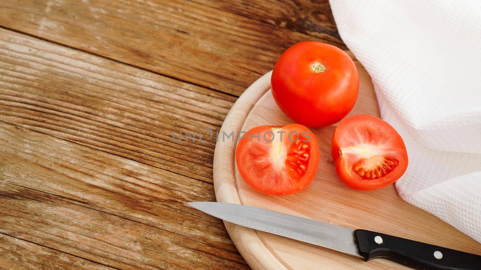 Slice Tomato on a Wooden Cutting Board. Knife and tomatoes on a wooden background. Cooking and kitchen concept