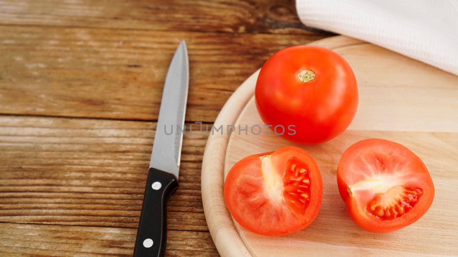 Slice Tomato on a Wooden Cutting Board. Knife and tomatoes on a wooden background. Cooking and kitchen concept