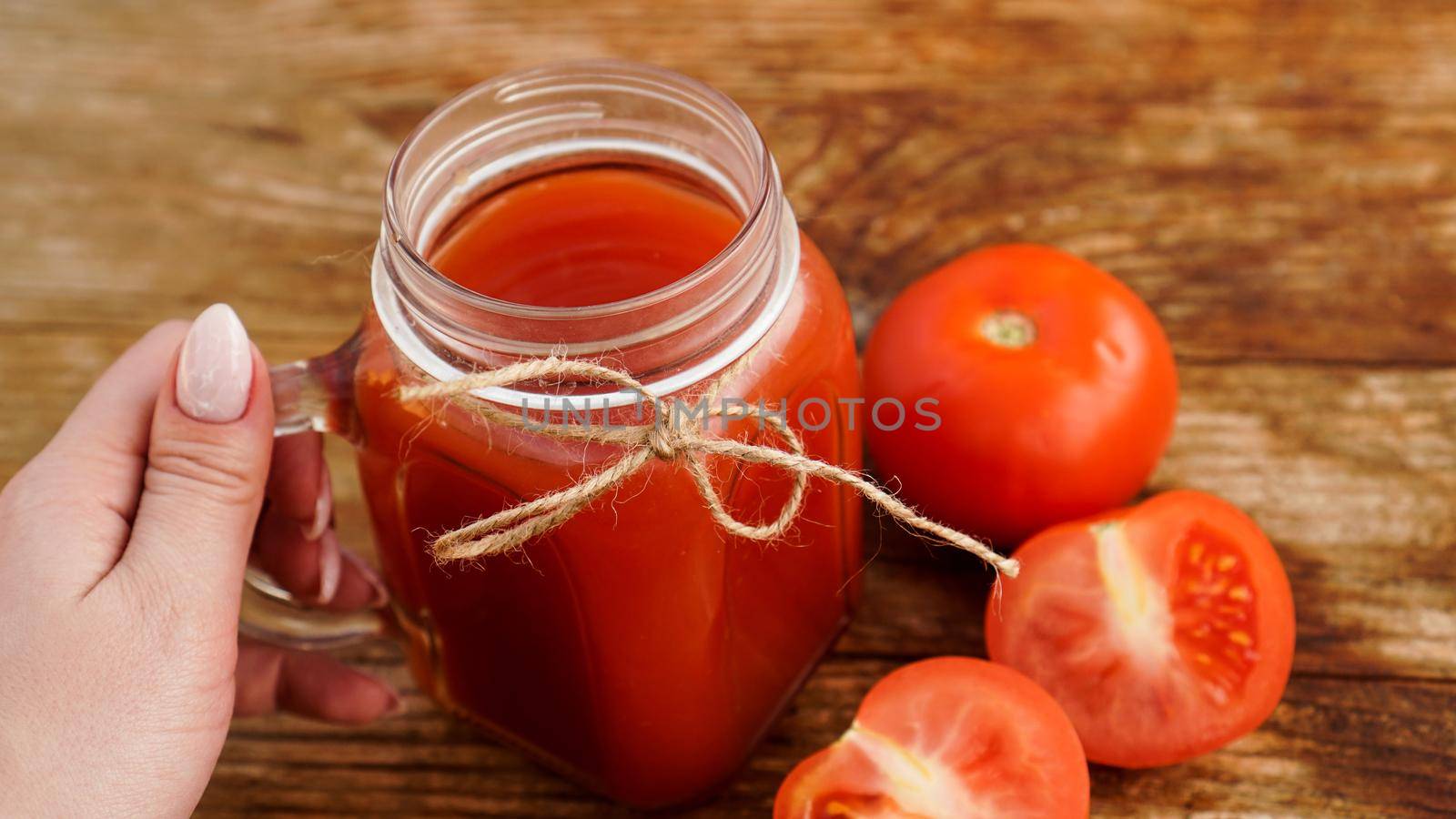 Female hand holds Glass of tomato juice on wooden table. Fresh tomato juice and chopped tomatoes on wooden board. Vertical photo