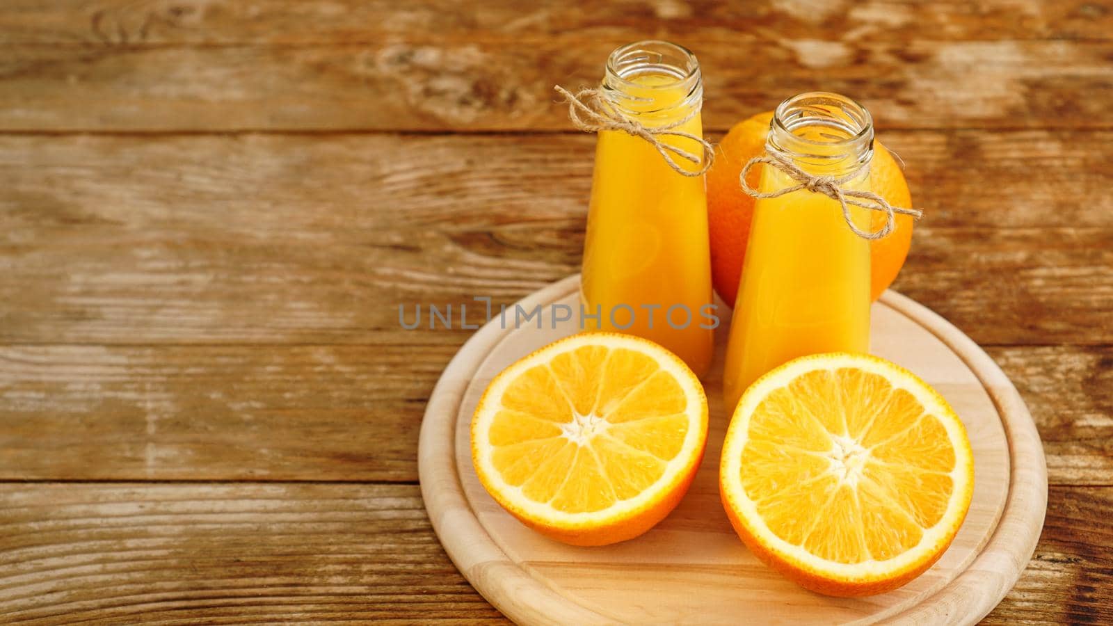 Fresh orange juice on wooden table on a wooden board. Sliced oranges and two bottles of juice