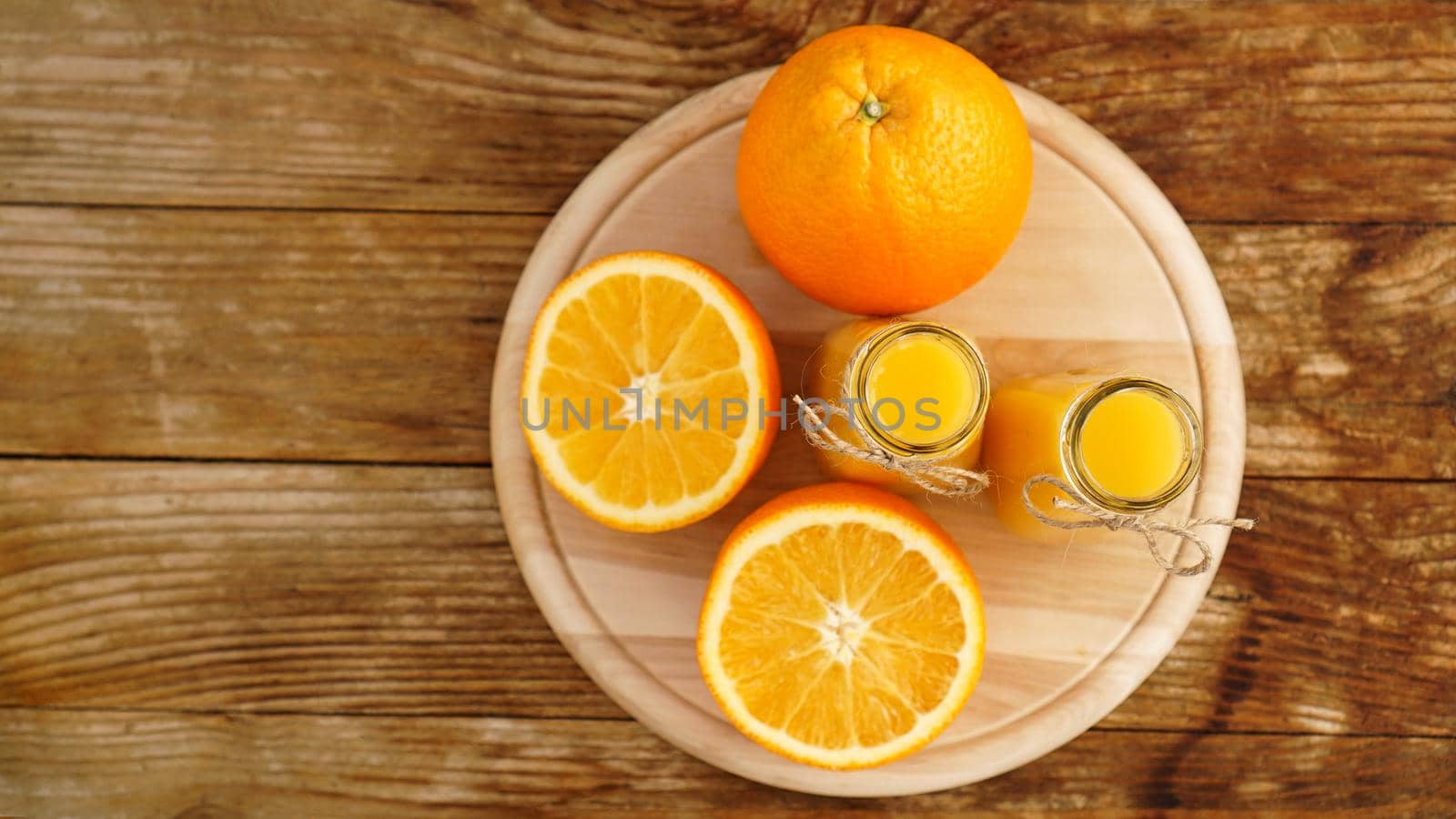 Fresh orange juice on wooden table on a wooden board. Sliced oranges and two bottles of juice. View from above