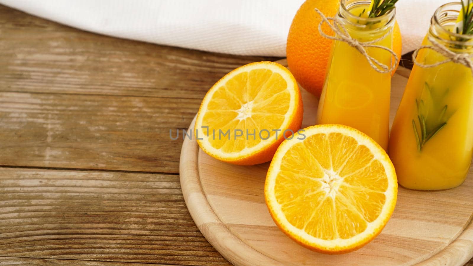 Orange juice in glass bottles. The juice is decorated with a sprig of rosemary. Juice on wooden background with white towel