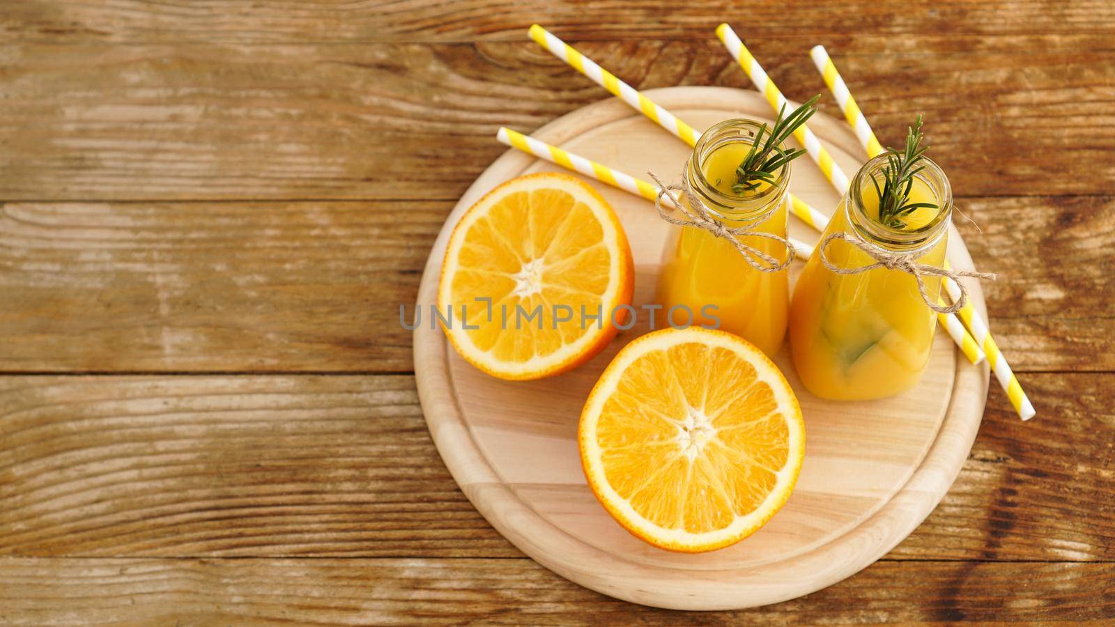 Orange juice in glass bottles. The juice is decorated with a sprig of rosemary. Juice on wooden background