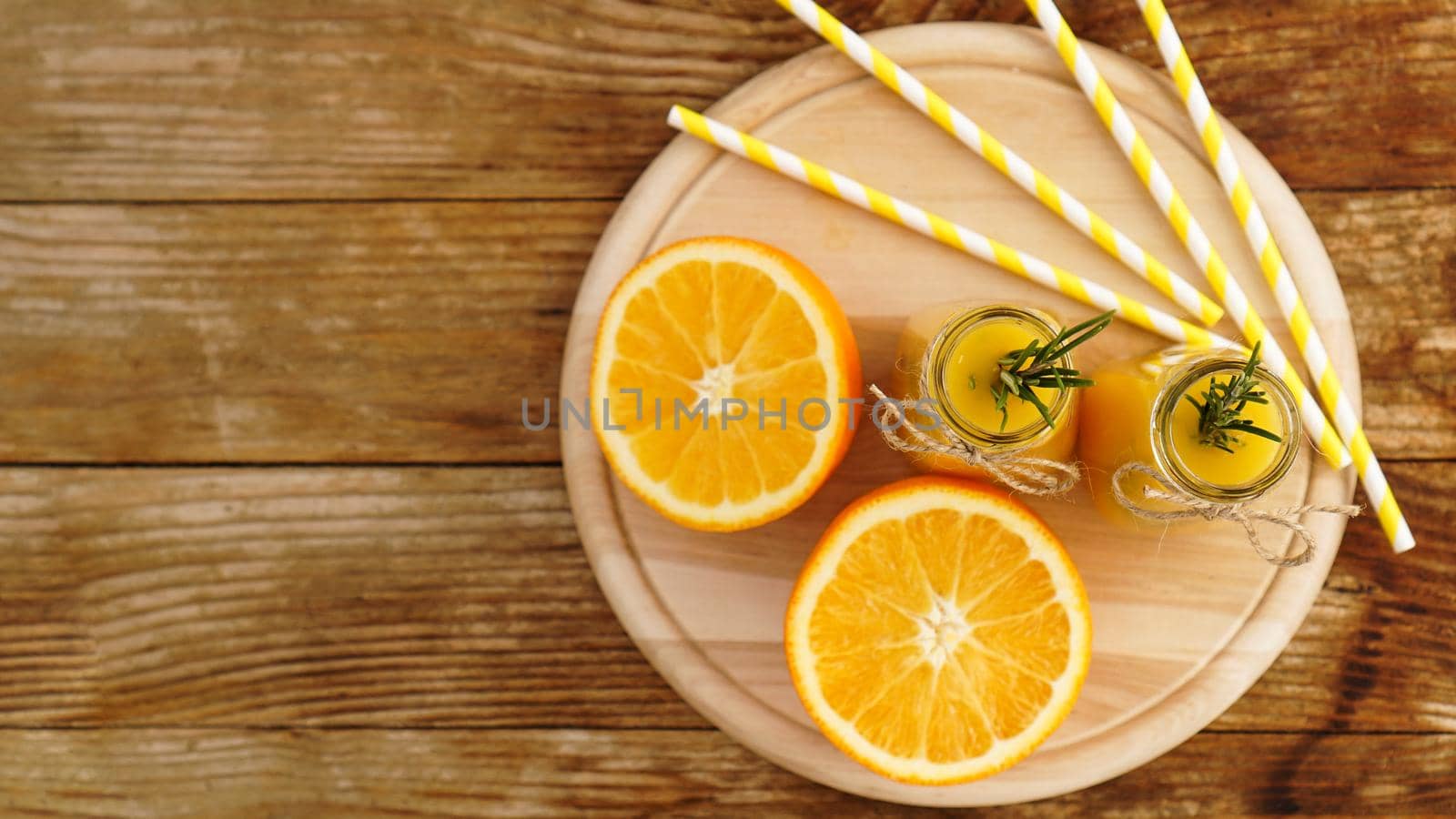Orange juice in glass bottles. The juice is decorated with a sprig of rosemary. Juice on wooden background. Top view