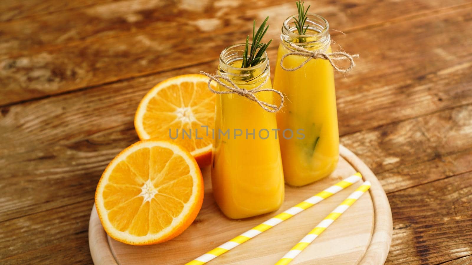 Orange juice in glass bottles. The juice is decorated with a sprig of rosemary. Juice on wooden background