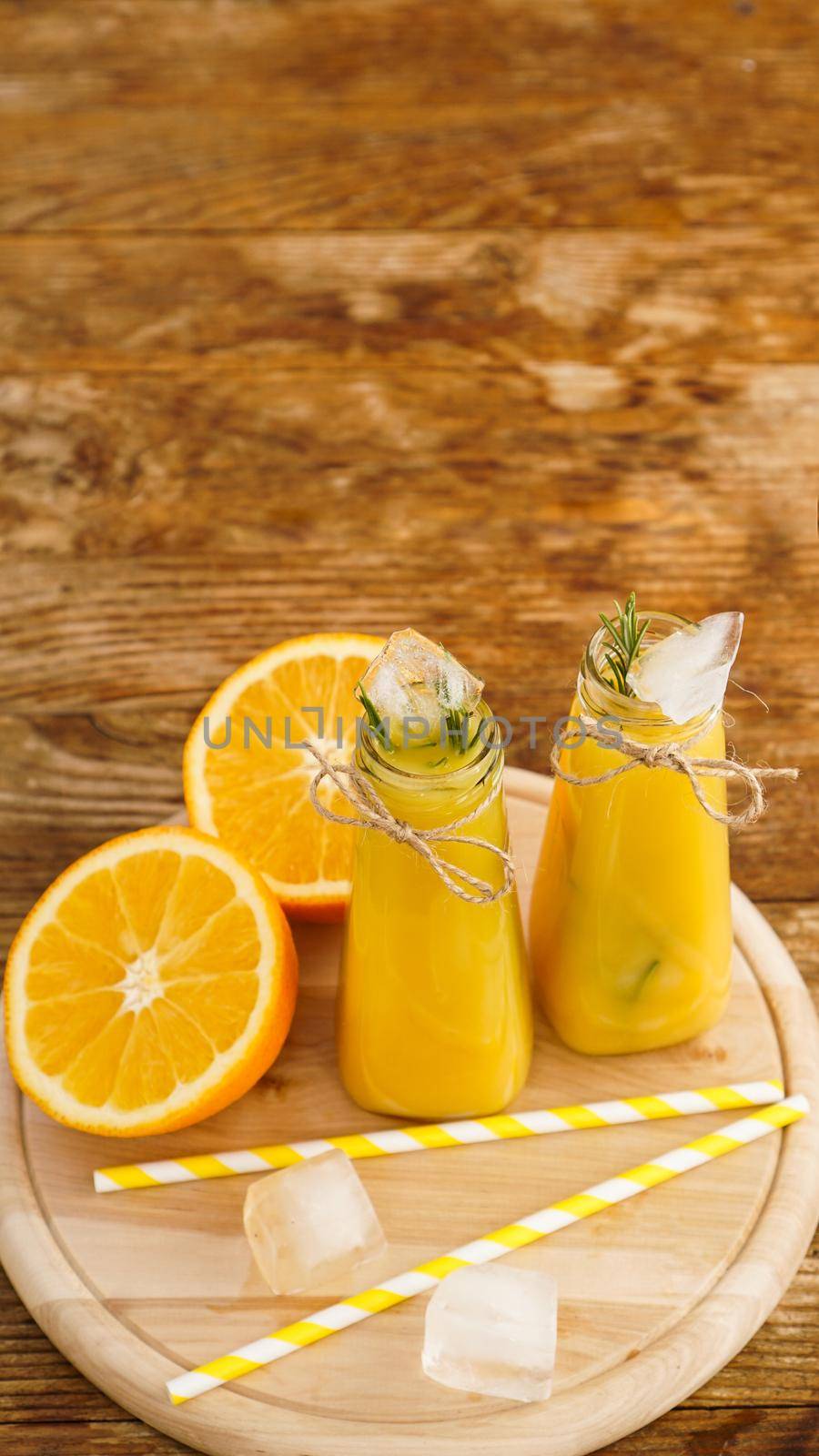 Orange juice on a wooden tray. Sliced orange and ice cubes. Snack at the resort, coolness on a hot summer day. Vertical photo