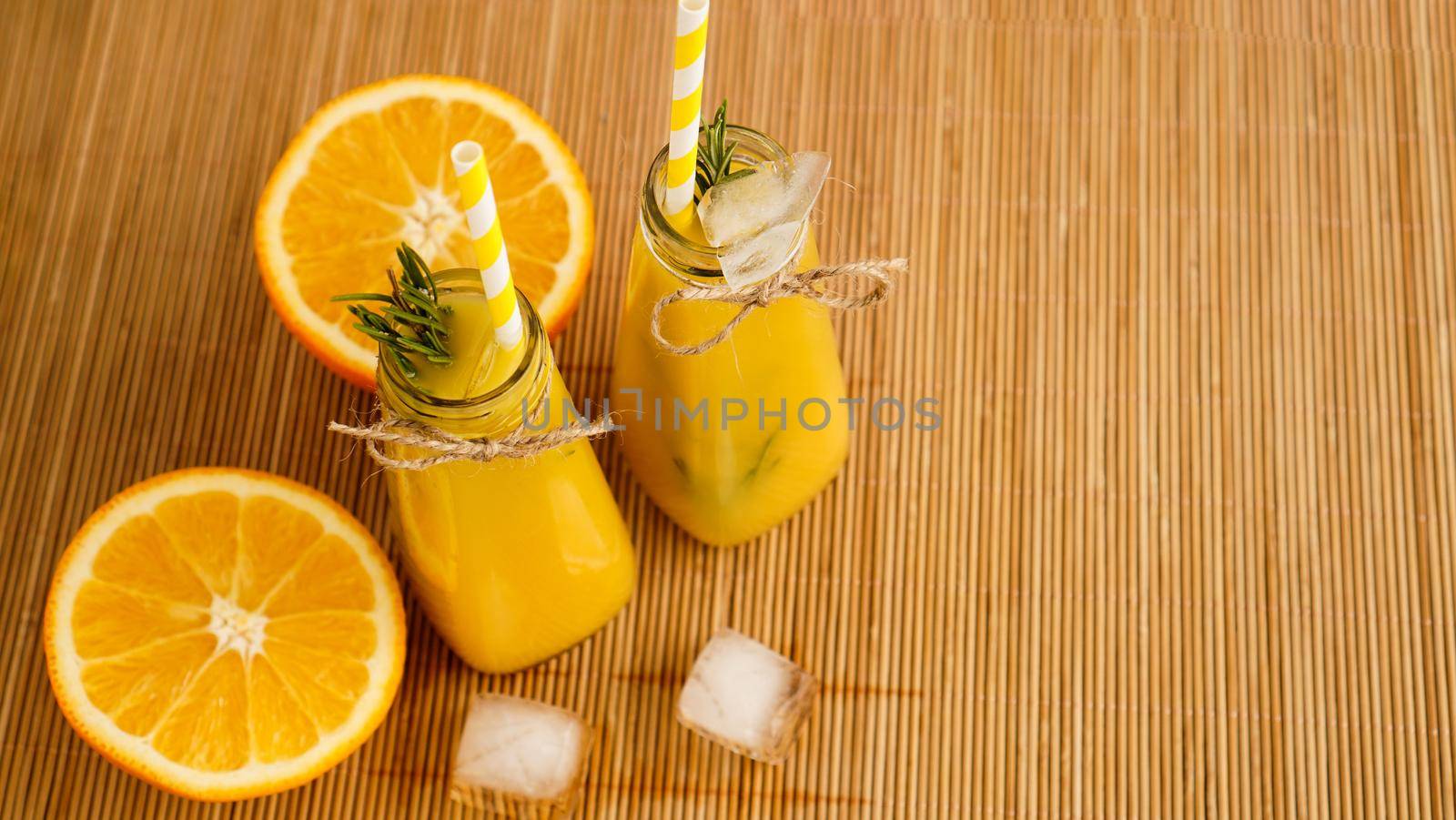 Orange juice bottles and paper straws. Icy drink on a sunny day. Pieces of ice in a bottle and on a bamboo napkin