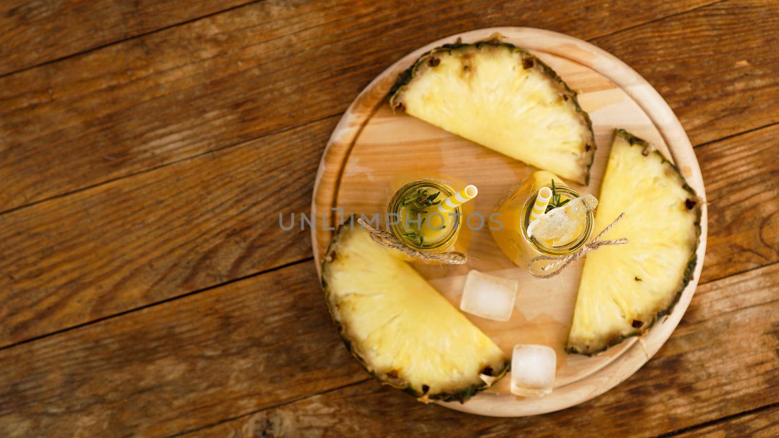 Fresh made Pineapple Juice with Ice in a small glass bottle on wooden background. Homemade drink. Top view
