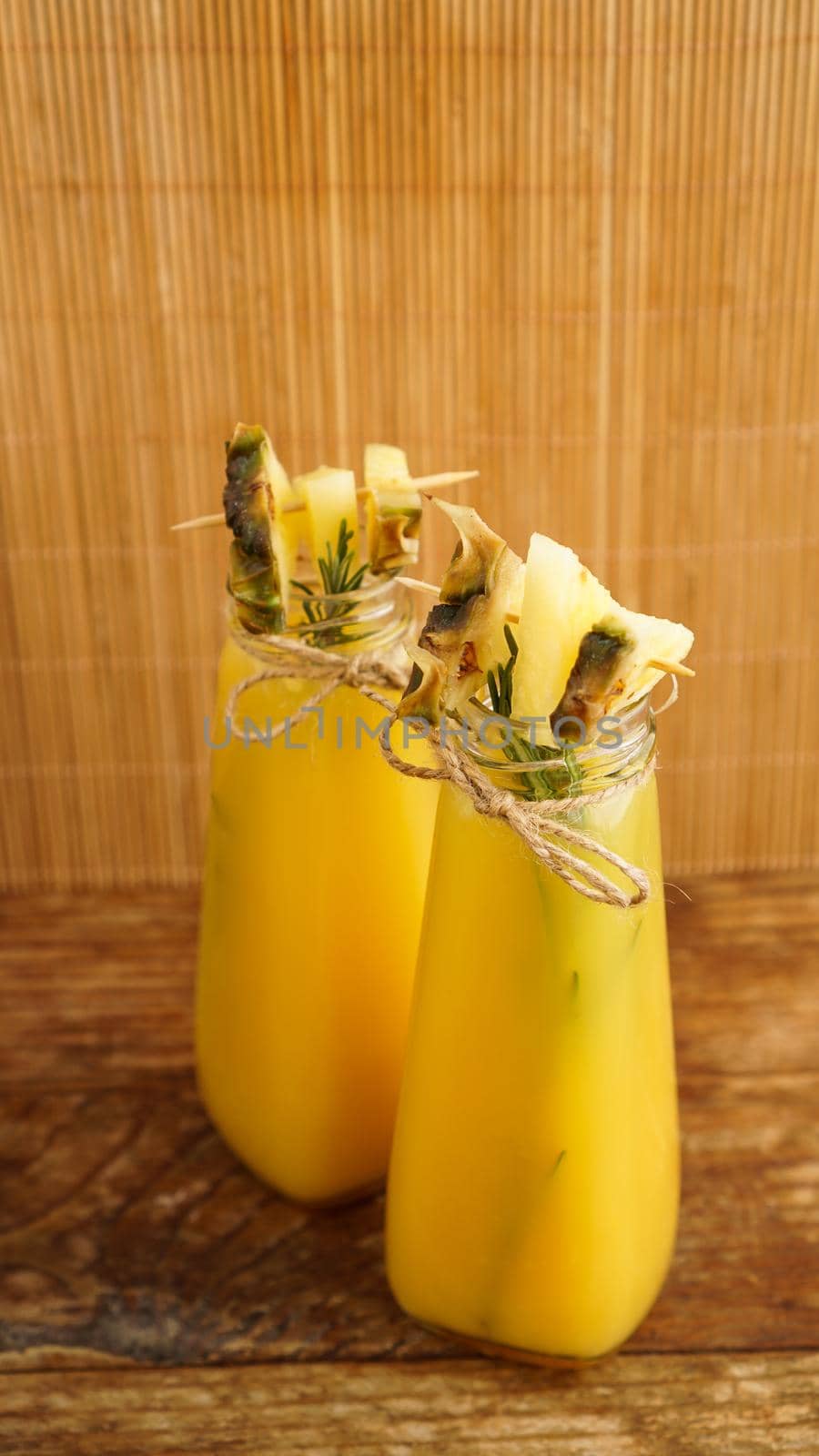 Pineapple juice in a small bottle. Pineapple slices decorate the drink. Juice on wooden background