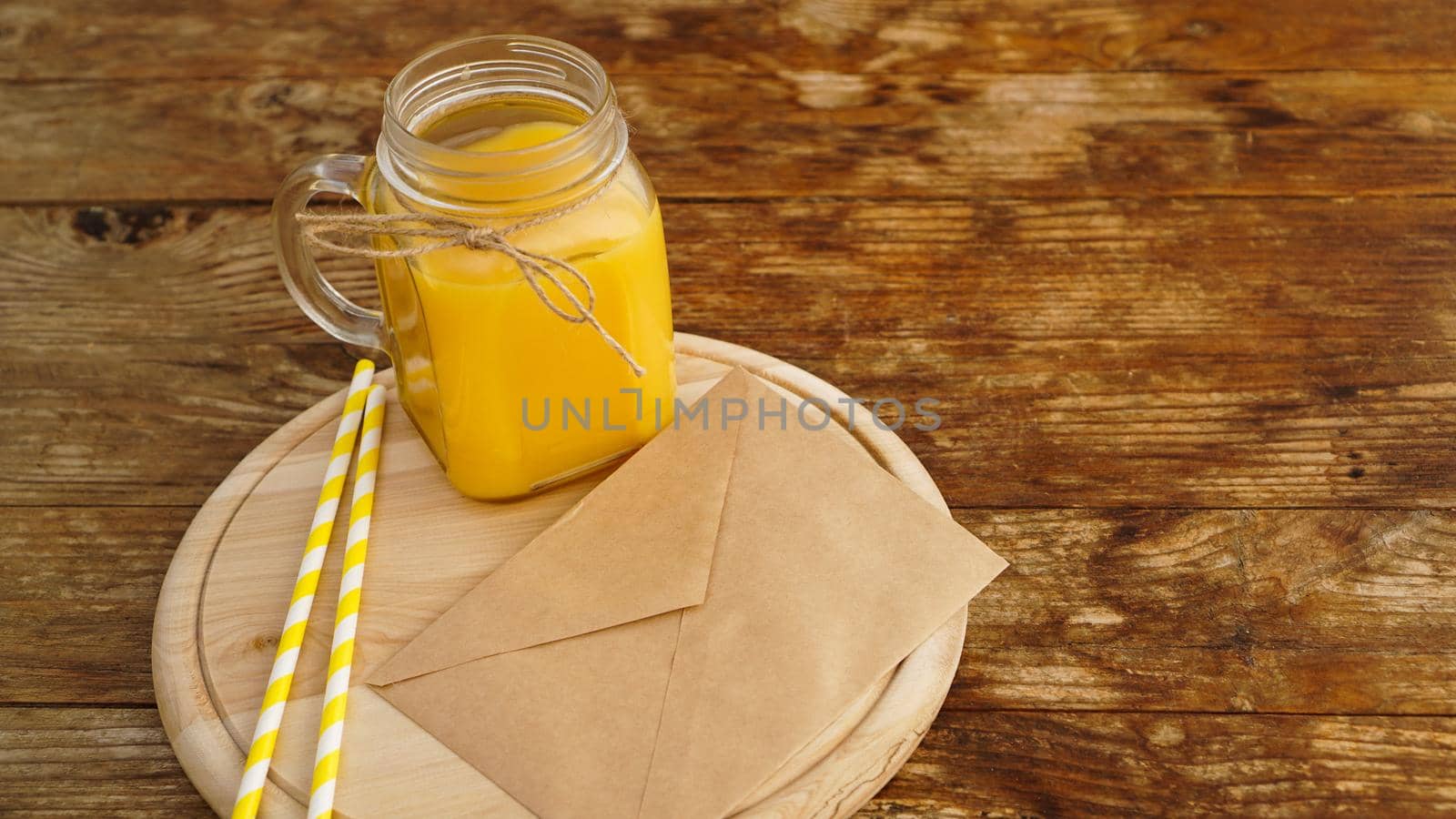 Orange juice in a glass jar on a wooden background. Envelope with a letter on a wooden board. Morning note and fruit breakfast