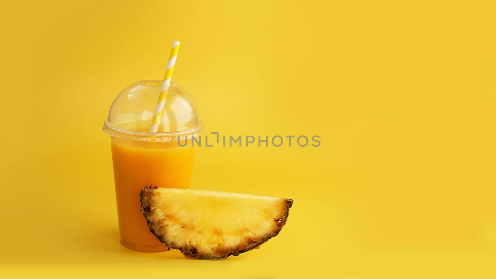 Pineapple juice in a plastic cup on yellow background. Tropical juice - summer banner