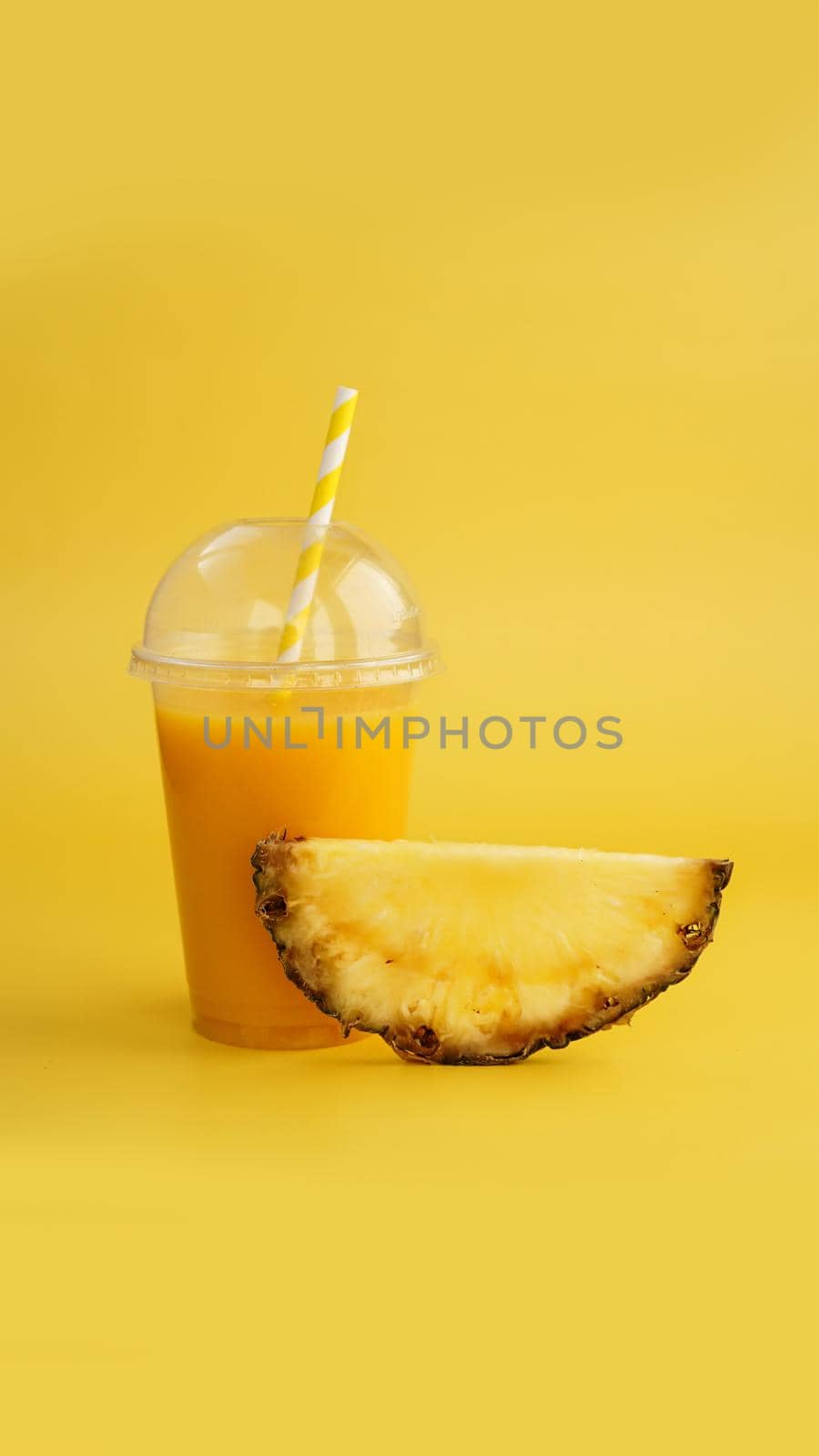 Pineapple juice in a plastic cup on yellow background. Tropical juice - summer banner