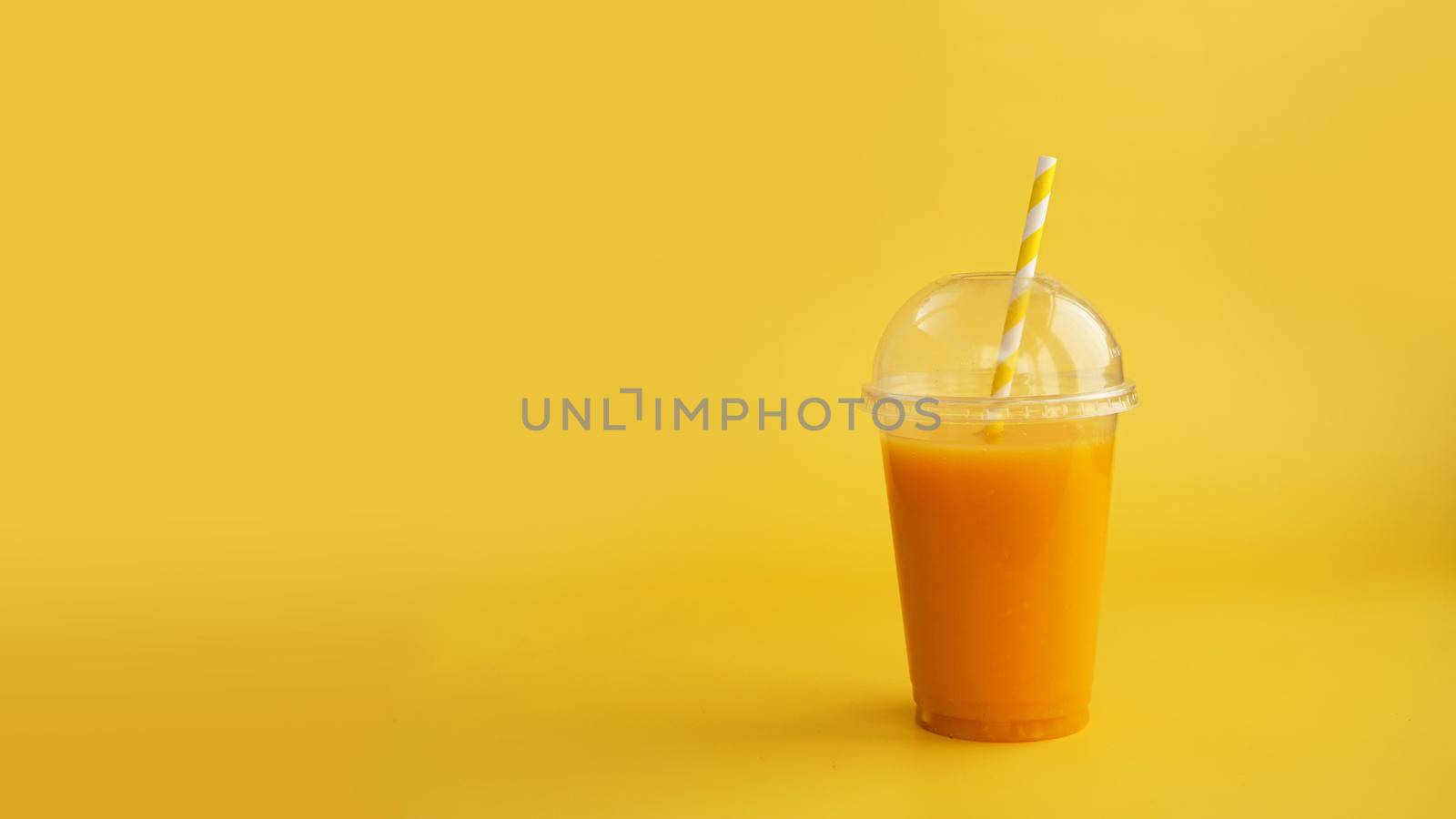 A plastic cup of orange drink. Natural juice or smoothies. Healthy food. Vegetarian or vegan food on yellow background