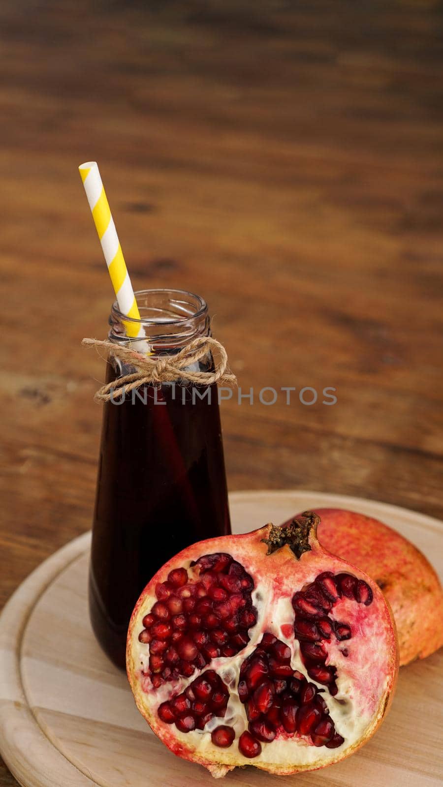 Ripe pomegranates with juice on wooden background. Red juice in small glass bottle on wooden background. Vertical photo