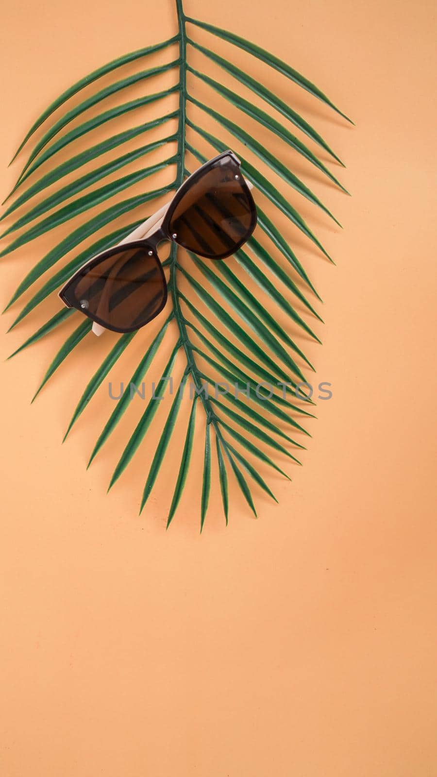 Sunglasses sale concept. Sunglasses on orange background with tropical leaves. Trendy Fashion summer accessories. Top view, vertical