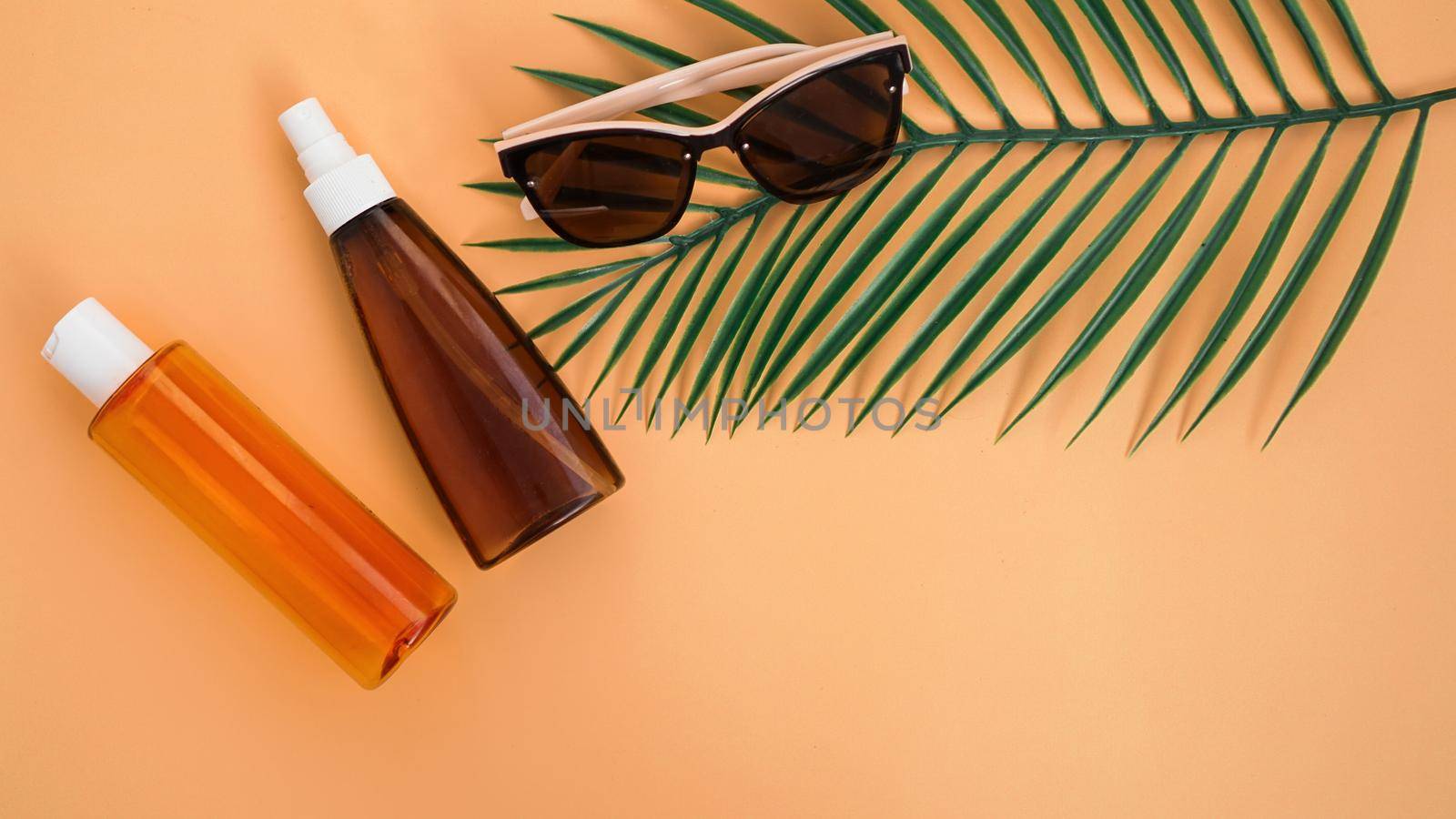 Sunglasses, sun lotion and palm leaves. Flat lay, top view on soft orange background